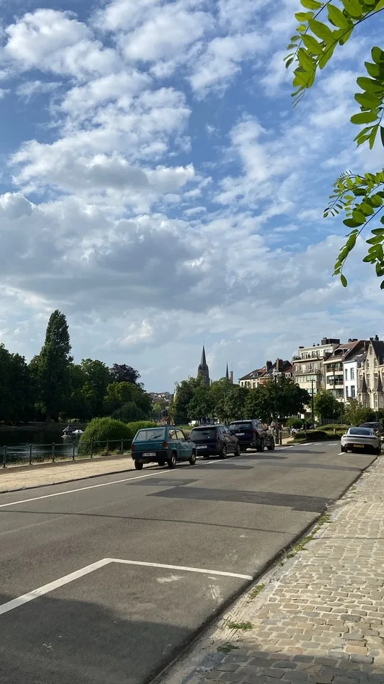 A tree-lined street along a pond in Brussels, a church spire behind the houses