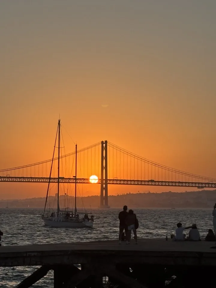Sunset behind the 25 de Abril bridge in Lisbon, a sailboat on the Tagus